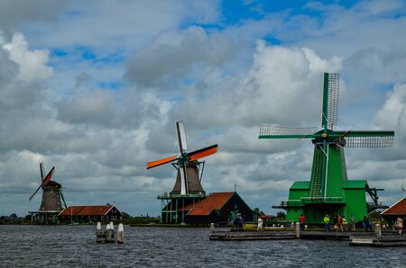 Zaanse Schans, Holland, August 2019. Northeast Amsterdam is a small community located on the Zaan River. View of the mills on the river bank, they stand out with their bright colors. Cloudy day.のeditorial素材