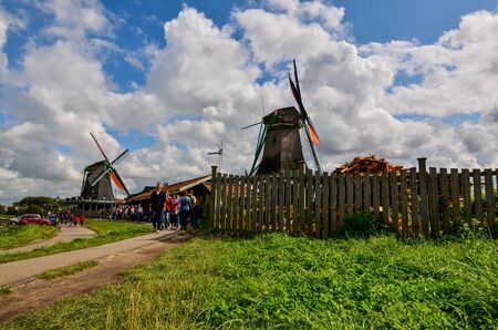 Zaanse Schans, Holland, August 2019. Northeast Amsterdam is a small community located on the Zaan River. View of the mills on the river bank, they stand out with their bright colors. Cloudy day.のeditorial素材