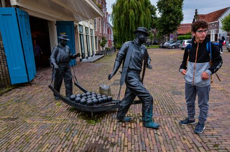 Edam, Netherlands, August 2019. The square where the characteristic cheese market takes place. A metal sculpture represents two men intent on carrying the cheese. A boy is watching her.のeditorial素材