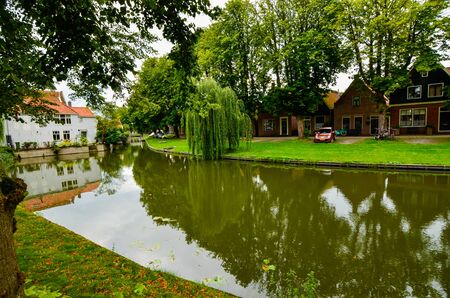 Edam, Netherlands, August 2019. One of the pretty canals of this city: the foliage of the trees is reflected on the water along the banks, pretty houses overlook the shore.のeditorial素材