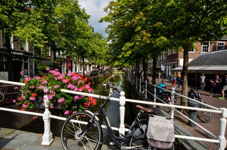 Delft, the netherlands, august 2019. The pretty and romantic canals. The aquatic plants create a green carpet, the bridges frame the flower boxes in warm and bright colors. Parked bikes.のeditorial素材