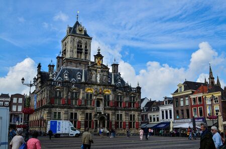 Delft, the netherlands, august 2019. The imposing town hall: on the dark stone facade stand out the red windows and the golden decorations. Blue sky with white clouds.のeditorial素材