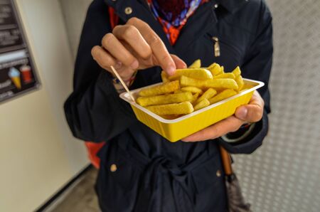 Oosterscheldekering, the Netherlands, August 2019. The main course at a street food kiosk: French fries. One portion is held up with one hand while the other hand grasps one to eat it.のeditorial素材