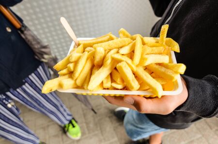 Oosterscheldekering, the Netherlands, August 2019. The main course at a street food kiosk: French fries. One portion is held up with one hand while the other hand grasps one to eat it.のeditorial素材