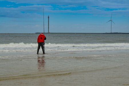 Holland, region of Zealand. August 2019. The wind turbines are the backdrop on the beach by the northern sea. A fisherman with a red jacket.のeditorial素材