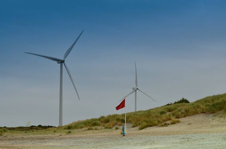 Holland, region of Zealand. August 2019. The wind turbines are the backdrop on the beach by the northern sea.のeditorial素材