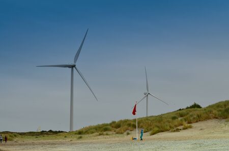 Holland, region of Zealand. August 2019. The wind turbines are the backdrop on the beach by the northern sea.のeditorial素材