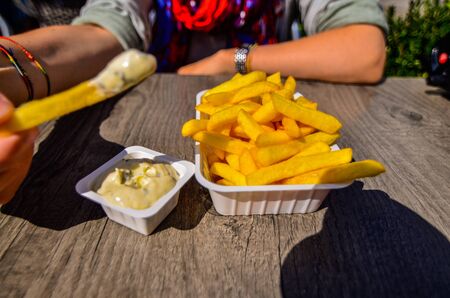 Bruges, Belgium, August 2019. A chip shop overlooking the touristy Markt square. A Caucasian woman is enjoying her chips with tartar sauce. Selective focus on potato chips.のeditorial素材