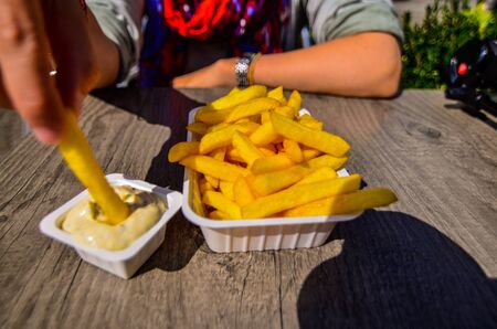 Bruges, Belgium, August 2019. A chip shop overlooking the touristy Markt square. A Caucasian woman is enjoying her chips with tartar sauce. Selective focus on potato chips.のeditorial素材