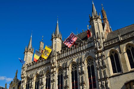 Bruges, Flanders, Belgium. August 2019. Burg square is one of the most important. The splendid town hall overlooks it. Detail of the spiers and flags that decorate the facade.のeditorial素材