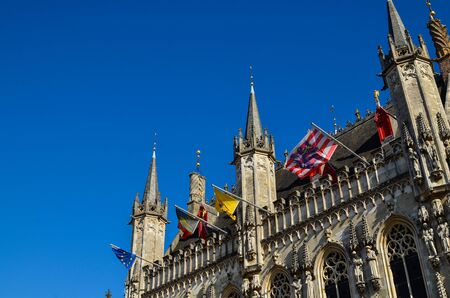 Bruges, Flanders, Belgium. August 2019. Burg square is one of the most important. The splendid town hall overlooks it. Detail of the spiers and flags that decorate the facade.のeditorial素材