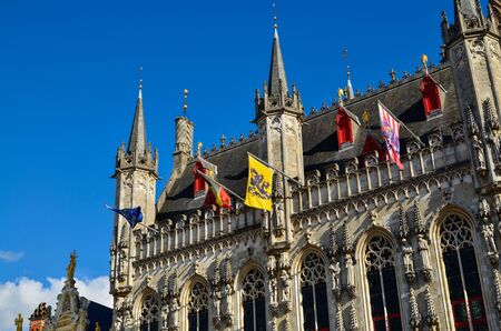 Bruges, Flanders, Belgium. August 2019. Burg square is one of the most important. The splendid town hall overlooks it. Detail of the spiers and flags that decorate the facade.のeditorial素材