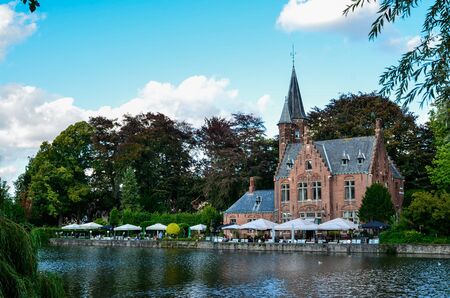 Bruges, Belgium. August 2019. The lake and minnewater park are the most romantic place. The body of water on which the red brick castle and the large trees with green foliage are reflected.のeditorial素材