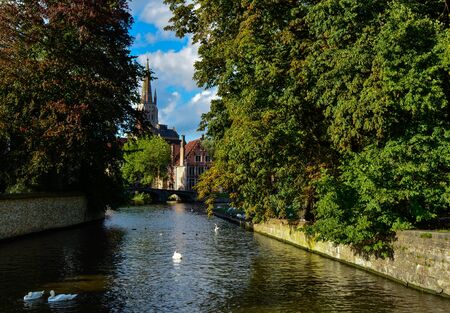 Bruges, Belgium. August 2019. View towards the historic center from the bridge with the Sashuis lock. The canal leads the eye towards the city. Large green foliage on the sides.のeditorial素材
