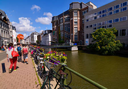 Ghent, Belgium, August 2019. Planters with brightly colored plants and some parked bikes stand out along the canals. People walk along the sidewalk that runs alongside the water.のeditorial素材