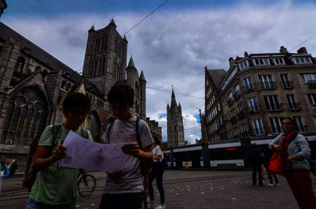 Ghent, Belgium, August 2019. Two boys consult the tourist map, behind them we recognize the church of St. Nicholas and the bell tower, the Beffroi.のeditorial素材