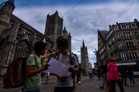 Ghent, Belgium, August 2019. Two boys consult the tourist map, behind them we recognize the church of St. Nicholas and the bell tower, the Beffroi.のeditorial素材