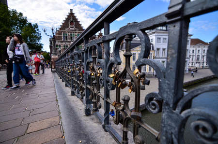 Ghent, Belgium, August 2019. Detail of the padlocks on the railings of the St. Michael bridge. People walking on the bridge, in the background the beautiful buildings overlooking the canal.のeditorial素材