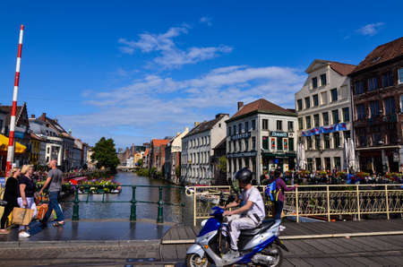 Ghent, Belgium, August 2019. Pleasant view of one of the canals in the historic center. The floristas color the railings of the bridge, people walk along it. Sunny day with blue sky and white clouds.のeditorial素材