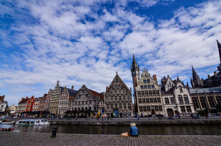 Ghent, Belgium, August 2019. Breathtaking cityscape: from the St. Michael bridge along the Graslei canal. One of the most beautiful postcards in the city. A lady stopped for a break, next to her bags.のeditorial素材