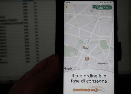 Turin, Piedmont, Italy. May 2020. Coronavirus. Order a home food delivery while working from home. The app of the Glovo company indicates the status of the order. In the background the pc screen.のeditorial素材