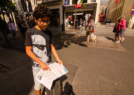 Antwerp, Flanders, Belgium. August 2019. A young tourist points his finger on the tourist map. Behind the main shopping street: a lot of people walk it.のeditorial素材