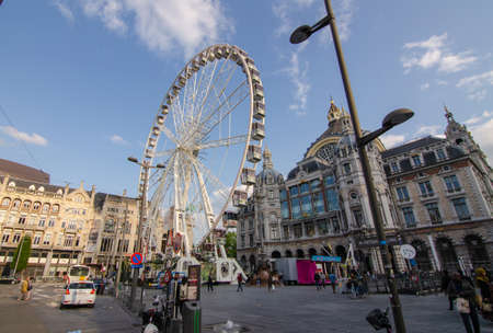 Antwerp, Flanders, Belgium. August 2019. Next to the railway station there is a large square where a Ferris wheel has been set up. Blue sky with white clouds. People.のeditorial素材