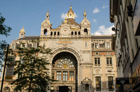 Antwerp, Flanders, Belgium. August 2019. The entrance facade of the imposing railway station. The late afternoon sun illuminates it with its warm light. Blue sky with white clouds.のeditorial素材