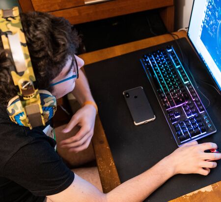 Caucasian boy with wavy brown hair and glasses wears gaming headphones. The look towards the monitor...