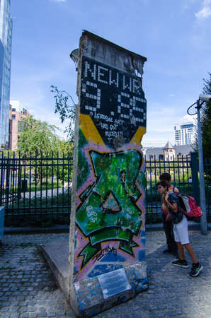 Brussels, Belgium, August 2019. A slice of the Berlin Wall at the entrance to the parliamentary offices. Some tourists are watching it.のeditorial素材