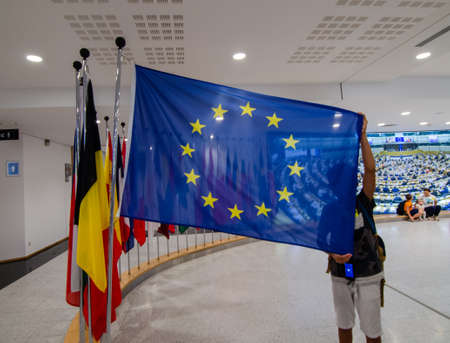 Brussels, Belgium, August 2019. At the headquarters of the European Parliament: the flags of the member states. A boy raises that of the European Union.のeditorial素材