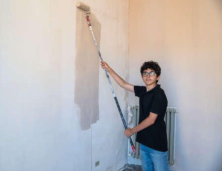 Renovate the walls of the house by painting them: the Caucasian boy with glasses passes the gray impregnated roller on the wall. A little color drips down the wall.の写真素材