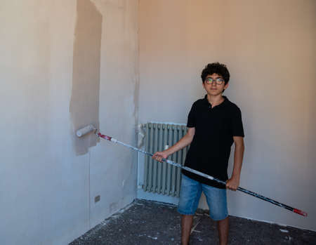 Renovate the walls of the house by painting them: the Caucasian boy with glasses passes the gray impregnated roller on the wall. A little color drips down the wall.の写真素材