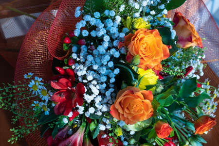 A beautiful composition of wildflowers and orange roses rests on a wooden chair. Close up shot: dew...