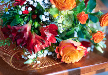A beautiful composition of wildflowers and orange roses rests on a wooden chair. Close up shot: dew drops are recognized.の写真素材