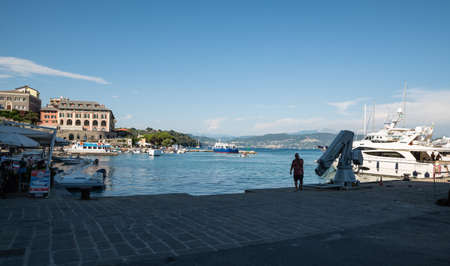 Portovenere, Liguria, Italy. June 2020. View of the promenade in front of the beautiful houses with colored facades: the tables of a restaurant, a tourist is talking on his cell phone.のeditorial素材