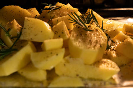 Close up shot of a pan inside the oven full of potatoes with salt, pepper and rosemary, the yellow light of the oven envelops them.の写真素材