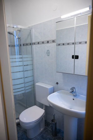 View of the interior of a bathroom from the entrance door. The yellow frame of the door is the frame: in evidence the mirror cabinet above the sink, on the left the toilet and the shower box.の写真素材
