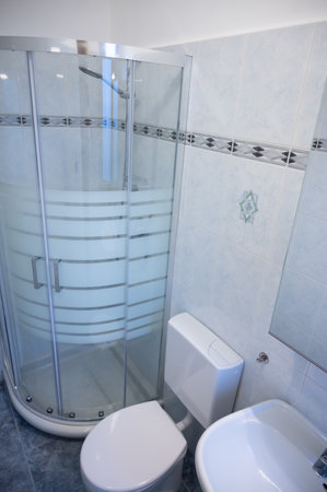 Interior of a narrow and long bathroom, the glass shower enclosure with metal frame is an eye-catcher. White ceramic sanitary ware.の写真素材