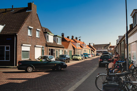 Westkapelle, The Netherlands, August 2019. A street in the town: the characteristic brick houses overlook the street. A couple is parking the bike.のeditorial素材