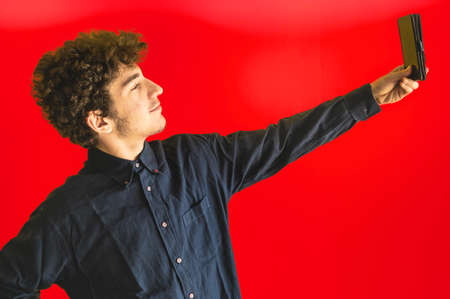 Cute brown curly haired caucasian boy on a yellow background, is posing with the smartphone camera to take a self-portrait. Copyspaceの写真素材