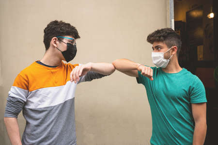 Young friends bump their elbows to greet in time pandemic. They use the mask to defend themselves from the  virus. Concept of social distance and friendship.の写真素材