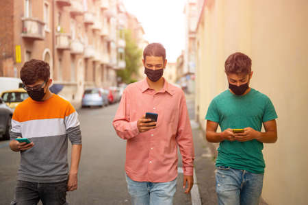 Friends group walking on city street with protective black face mask using the smartpjone. Pandemic...