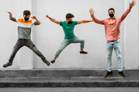 Young people jumping outdoor during  virus outbreak. Happy friends wearing face protective masks and having fun together. Social distancing,happiness concept, new normal. Millennials lifestyle.の写真素材