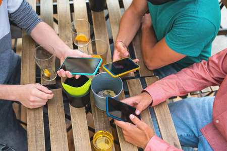 Close-up of young people using smart phones at the table after drinking glasses of soft drinks. Modern technology and youth lifestyle concept.の写真素材