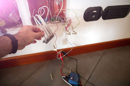 A telephone junction box has been opened: a line test tool has been connected with clamps. The technician's hand checks the other cables present.の写真素材