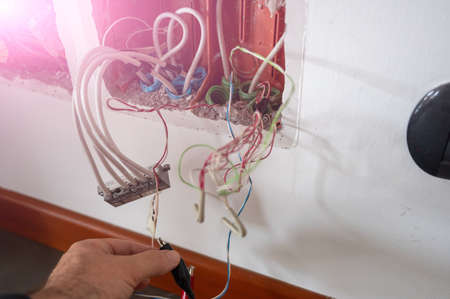 A telephone junction box has been opened: a line test tool has been connected with clamps. The technician's hand checks the other cables present.の写真素材