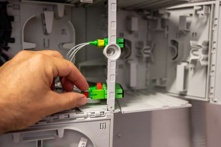A technician at work: close up shot of the hand checking the cabling of the optical fibers inside the distribution box.の写真素材