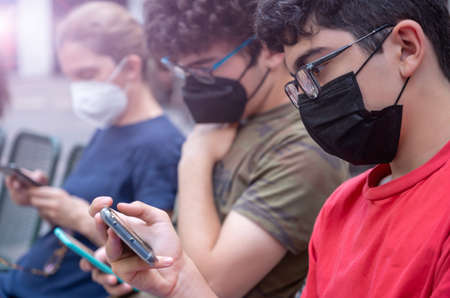 A middle-aged woman and her children are consulting their smartphones for a while. Everyone has a mask to defend themselves from the virus. Concept of new normal and use of technology.の写真素材