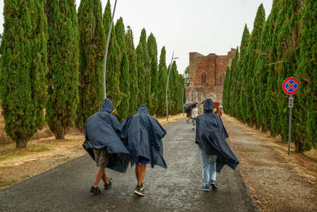 San Galgano, Chiusdino, Italy. August 2020. Conceptual image of meteorological variability: a group of tourists try to protect themselves from a summer storm with plastic capes.のeditorial素材